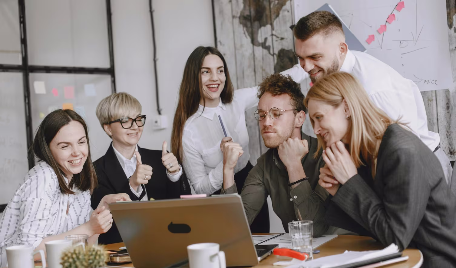 Group of coworkers celebrating success while gathered around a laptop in a modern office.