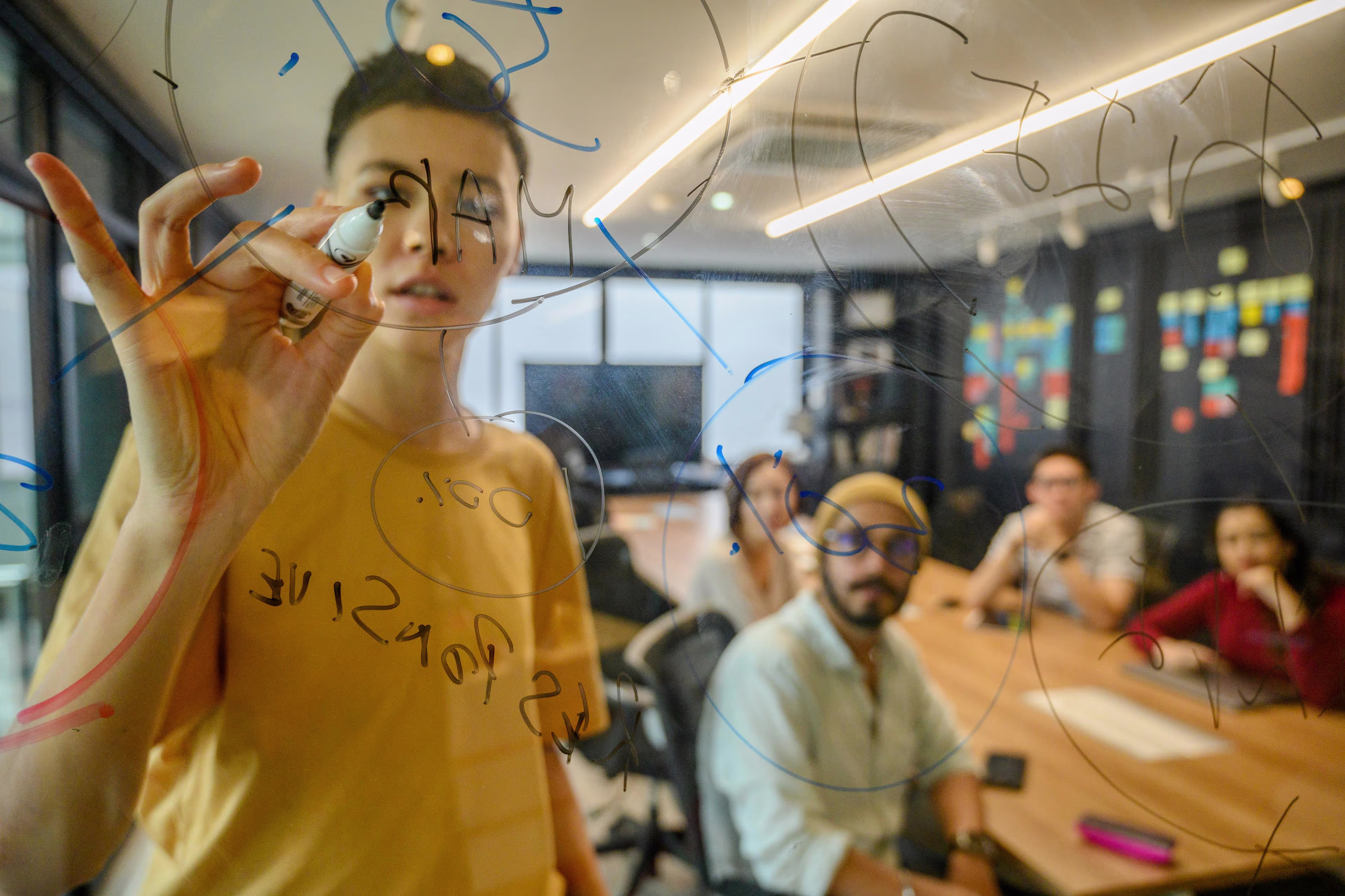 Team members brainstorming and writing ideas on a glass board in a modern office meeting room